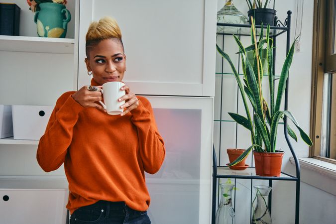 Black woman drinking from coffee mug in a bright home