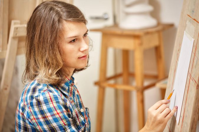 Female using pencil to draw on easel