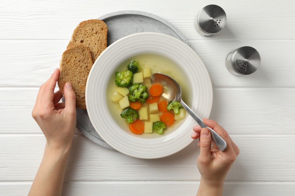 Looking down at person’s hands with spoon in vegetable soup