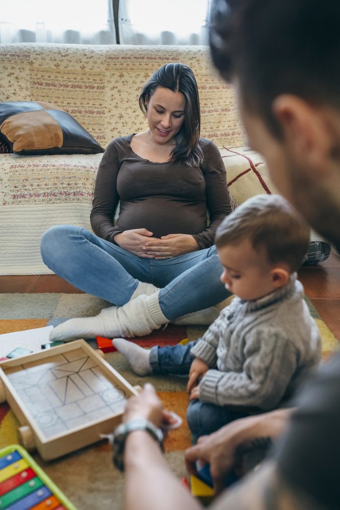 Father playing with toddler while the mother is looking her belly