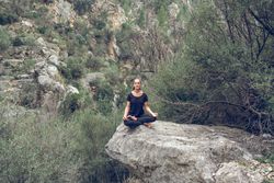young meditating woman sitting on stone in Padmasana pose
