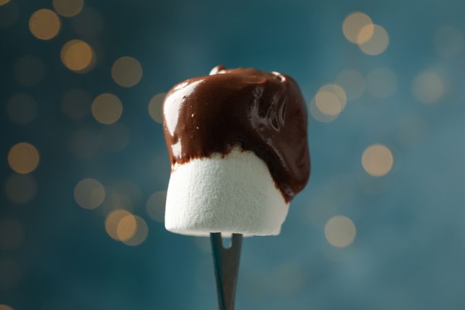 Marshmallow in chocolate against blue background with blurred lights