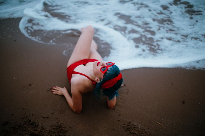 Relaxed woman in bright stylish swimsuit lying on sandy beach