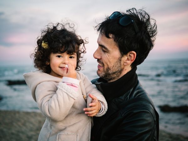 father holding little daughter at the beach