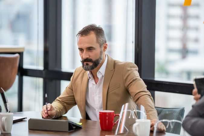 Bearded man with tablet on desk in bright cowering space