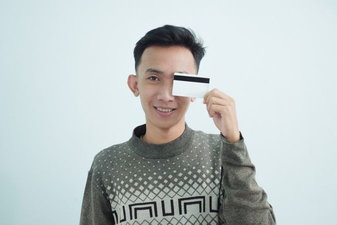 Playful Asian young men in sweater and holding blank credit card