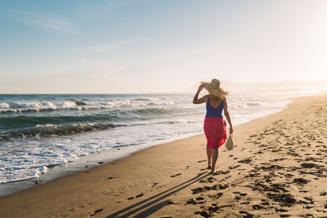 Woman holding hat and walking along seaside