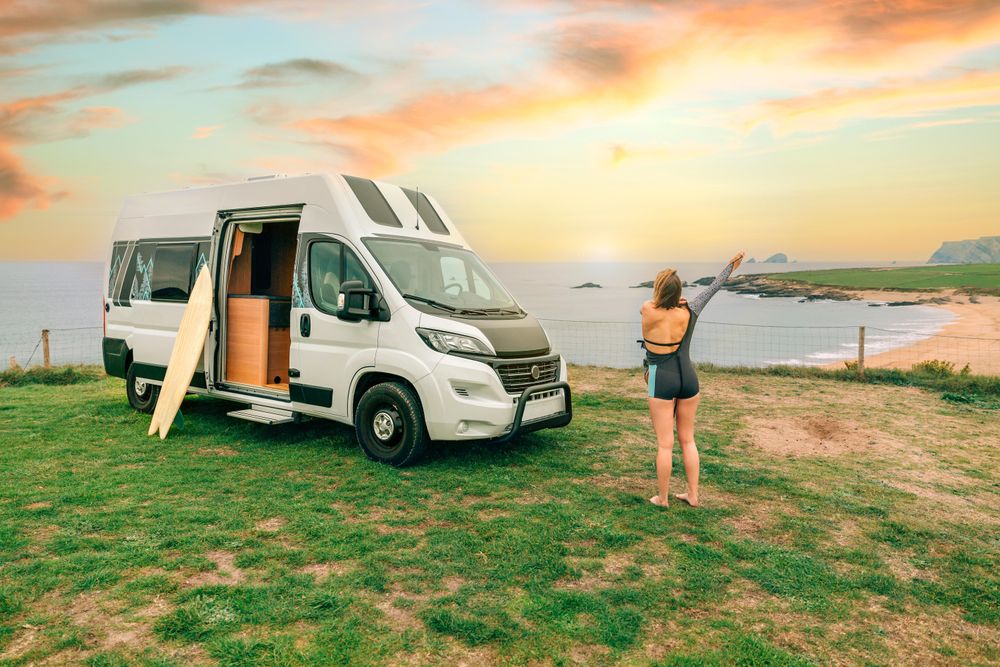 Female putting on wetsuit outside of motorhome parked on the coast
