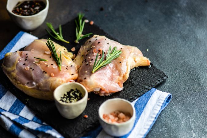 Raw chicken with rosemary sprig on kitchen slab with seasoning