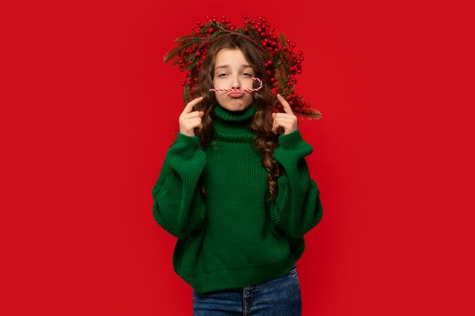 Young girl in green sweater balancing candy cane mustache
