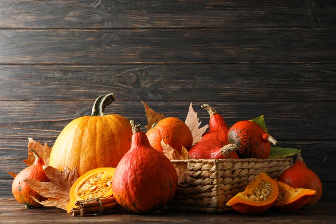 Straw basket, pumpkins, leaves and cinnamon on wooden background, copy space