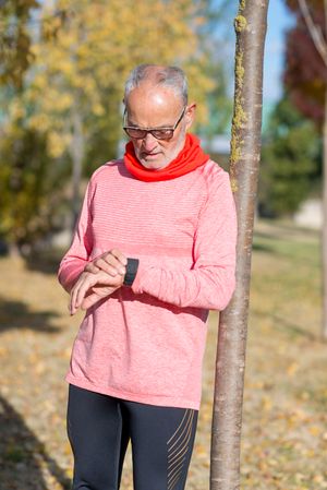 Grey haired man leaning on tree and looking at watch