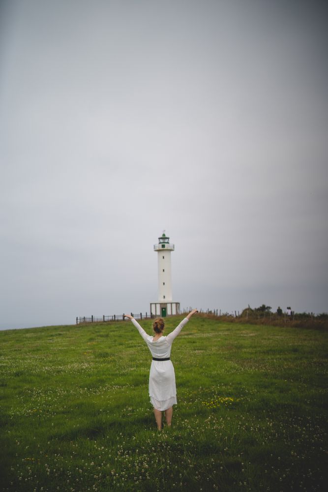 Woman walking in green meadow near lighthouse