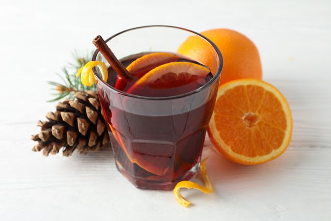 Glass of tasty mulled wine with orange on plain wooden background, space for text