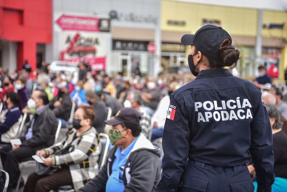 Back view of police standing bear people with facemasks sitting on chairs outdoor waiting for vaccination