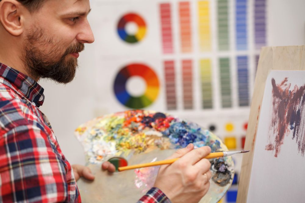 A man holds a bristle brush and a wooden palette with oil paints
