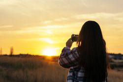 Young woman taking photos with analog camera in the field at sunset