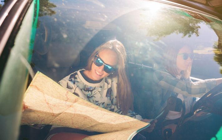 Happy young woman looking at a map inside of car