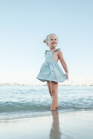 Happy little girl standing in sea on beach