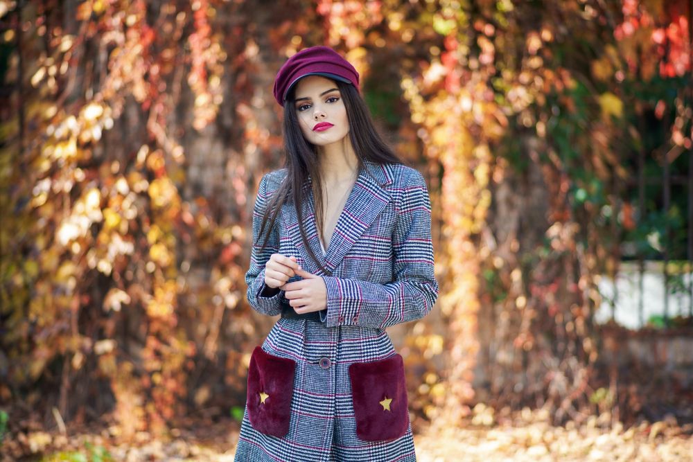 Female in warm winter clothes standing in park with colorful autumn leaves on sunny day