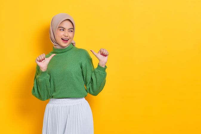 Happy woman in headscarf pointing both her thumbs towards herself