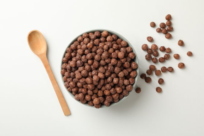 Spoon and bowl with corn balls on neutral background, top view
