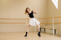 Ballerina in shoes and tutu, holding shoulder in modern dance