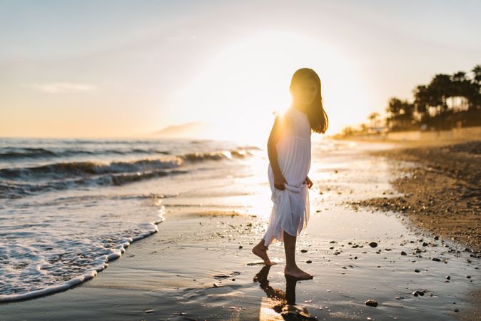 Adorable girl walking and looking at camera on seaside at sunset