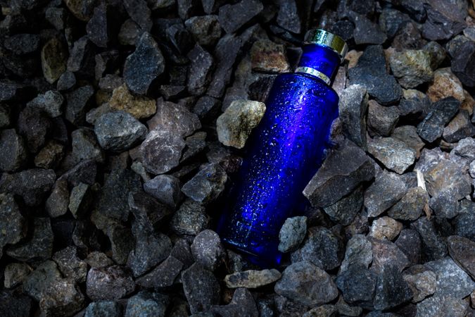 Wet blue perfume bottle mock up laying in grey rocks