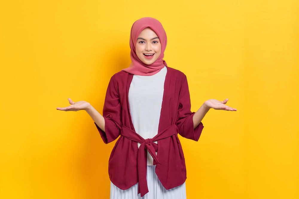 Woman in red headscarf smiling with both hands up, questioning