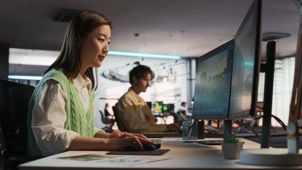 Asian Woman Using Desktop Computer And Designing In 3D Modelling Software Unique World And Characters For Survival Video Game In Diverse Office.