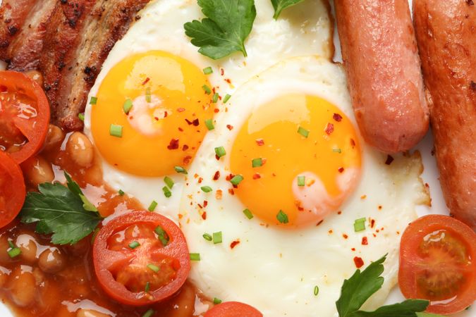 Top view of two eggs sunny side up, with seasoning, sausage and tomatoes