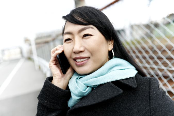 East Asian woman in red scarf and dark jacket having a phone call outdoor