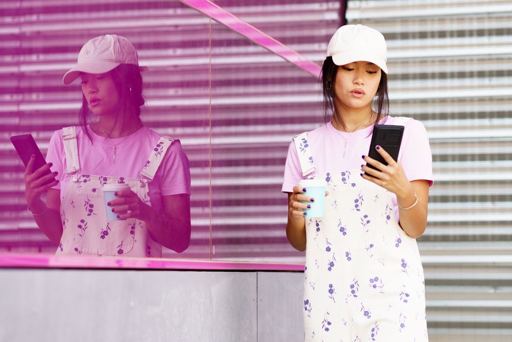Serious female in floral overalls checking her smartphone with a takeaway coffee