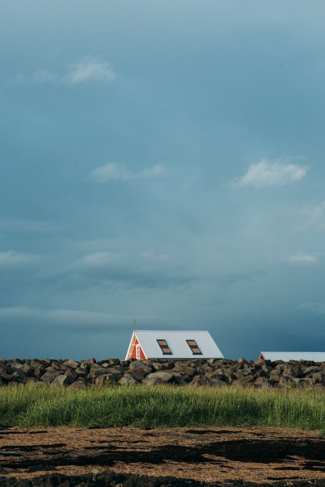 Small house in green filed under cloudy sky