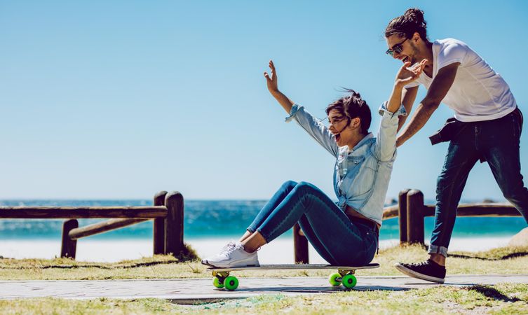 Happy woman sitting on skateboard with boyfriend pushing her
