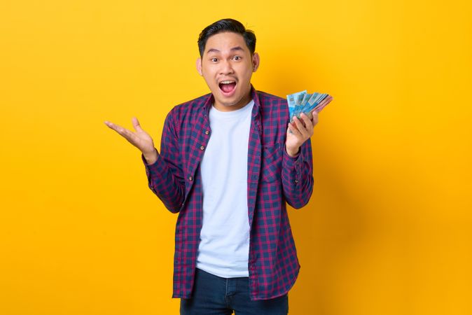 Thrilled man holding cash in yellow studio