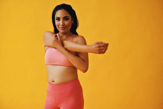 Hispanic woman in yoga clothes stretching her arm in yellow room, copy space
