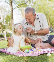 Grandfather and Granddaughter Coloring Easter Eggs on Blanket At Park