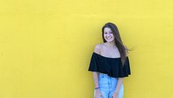 Beautiful woman leaning on yellow wall smiling on a sunny day