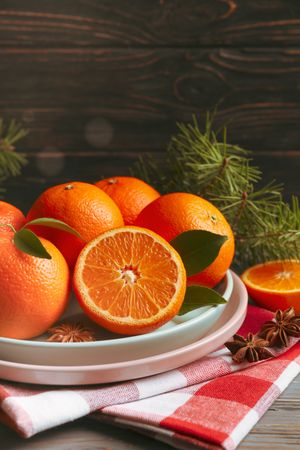 Plates with mandarins, pine branches, napkin and cinnamon on wooden background