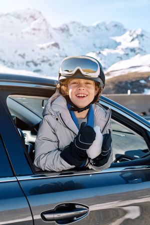 Cheerful boy leaning out window of car on winter day