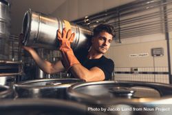 Handsome male worker moving beer keg while wearing rubber gloves 0Kz3yb