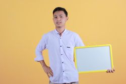 Portrait of a young man in yellow backdrop holding a blank note board