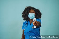 Portrait of Black medical professional in face mask dressed in scrubs with a digital thermometer 5aZKG4