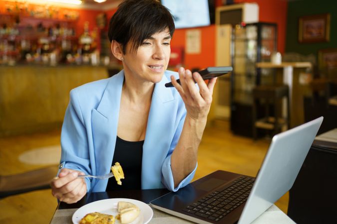 Woman sitting in cafe speaking on phone with laptop and slice of cake
