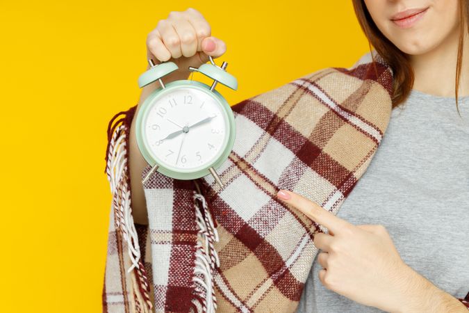 woman with plaid holds alarm clock on yellow background