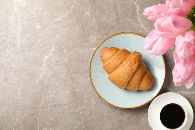 Plate with croissant on grey background with tulips and cup of coffee, top view with space for text