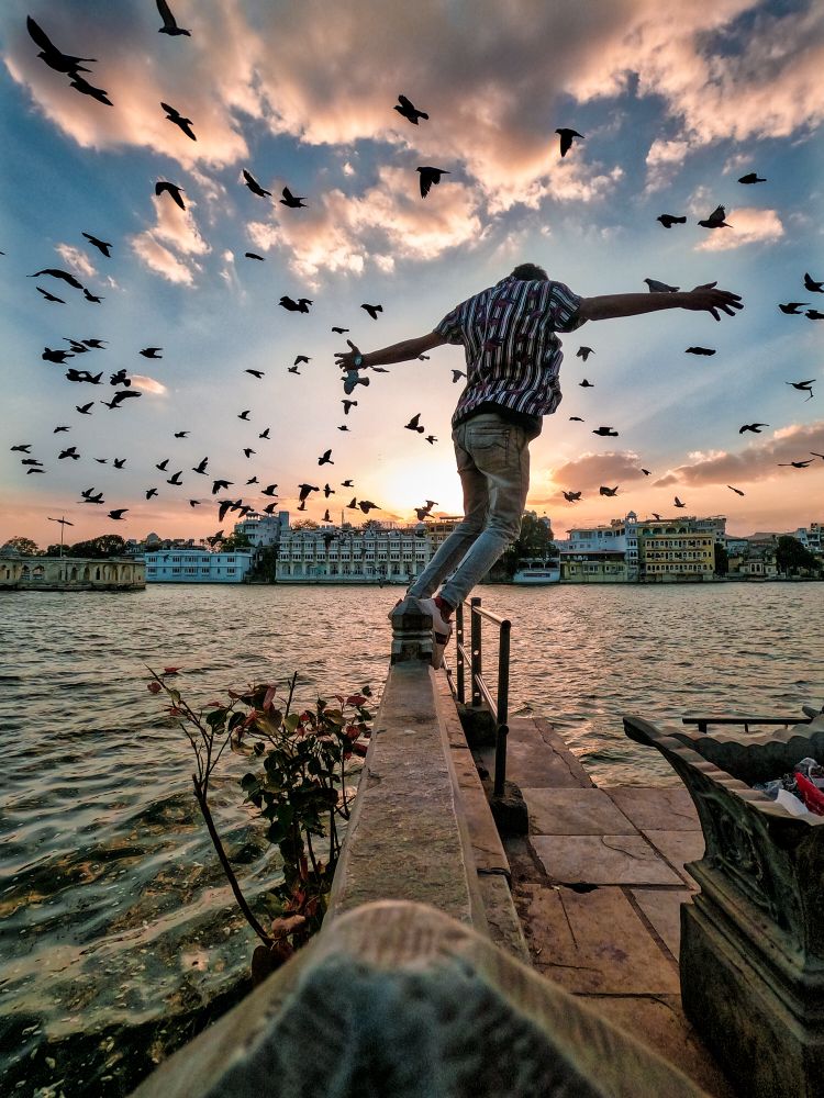 Back view of man balancing on a wall by riverside at sunset in India