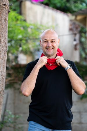 Man smiling and looking at camera with red bandana around his neck standing outside